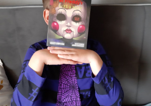 Praca Pawła Maciejewskiego - Zdjęcie przedstawia chłopca w granatowej koszuli z krawatem. W miejsce głowy przyłożono książkę „Five Nights at Freddys.
